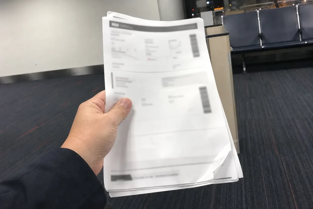 En hand håller i hopvikta flygbokningsbekräftelser vid en flygplatsgata, ett tecken på att kriget kan radera flygbolagens ...