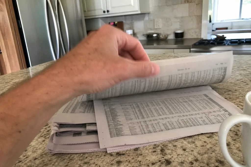 En hand bläddrar i finanstidningar med aktiekurser vid morgonljus, kopplat till Dagens rekar: Flera höjningar för rapportv...