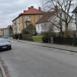 Bostadsgata i svenskt villaområde en mulen eftermiddag, person promenerar hund i bakgrunden, relevant för bostadsprisförvä...