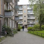 Bostadsgård mellan flerfamiljshus där en person går mot en entré, vardaglig miljö kopplad till fastighetsförvaltare uppköp