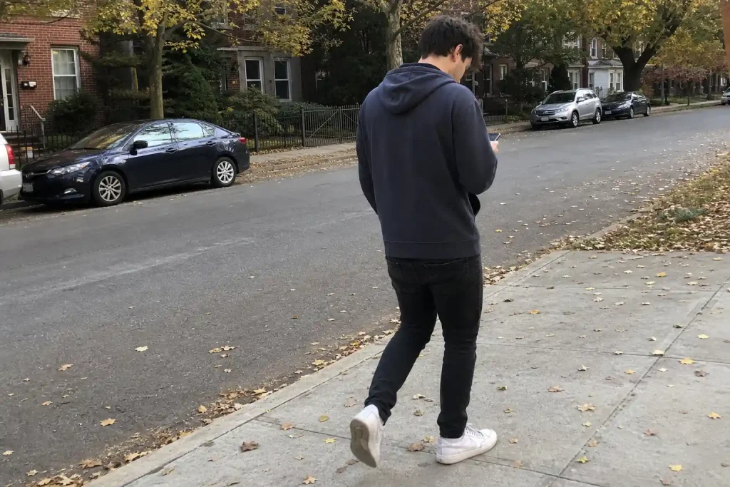 Ung man i huvtröja går på trottoaren och tittar ner i mobilen, relaterat till hög förekomst av spelproblem bland unga elit...