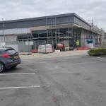 En Lidlbutik under byggnation med byggställningar och en arbetare på plats, del av pågående Lidl butiksexpansion.