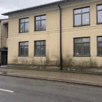 Fasad på kontorsbyggnad med synlig mögelskada kontorsfastighet, inspektör med anteckningsblock vid entrén.