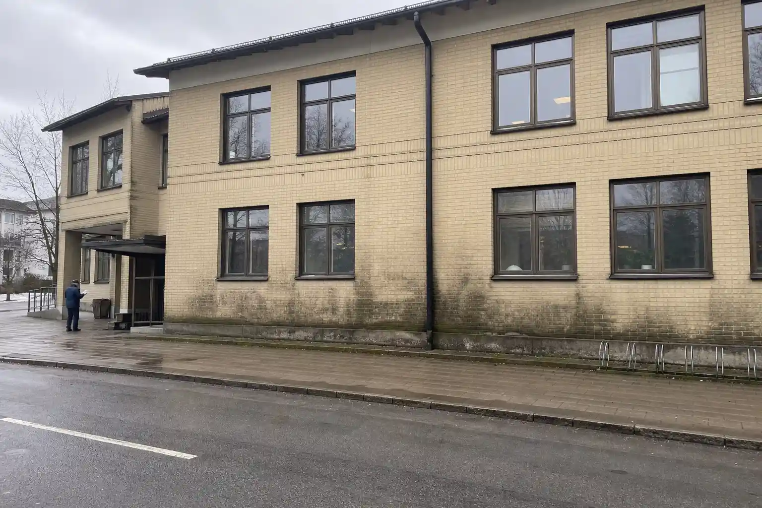 Fasad på kontorsbyggnad med synlig mögelskada kontorsfastighet, inspektör med anteckningsblock vid entrén.