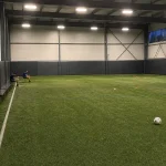 Tom inomhusarena för fotbollsträning med några unga spelare vid bänken i bakgrunden, relaterat till spelproblem bland unga...