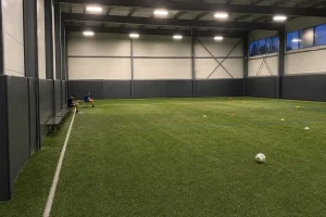 Tom inomhusarena för fotbollsträning med några unga spelare vid bänken i bakgrunden, relaterat till spelproblem bland unga...