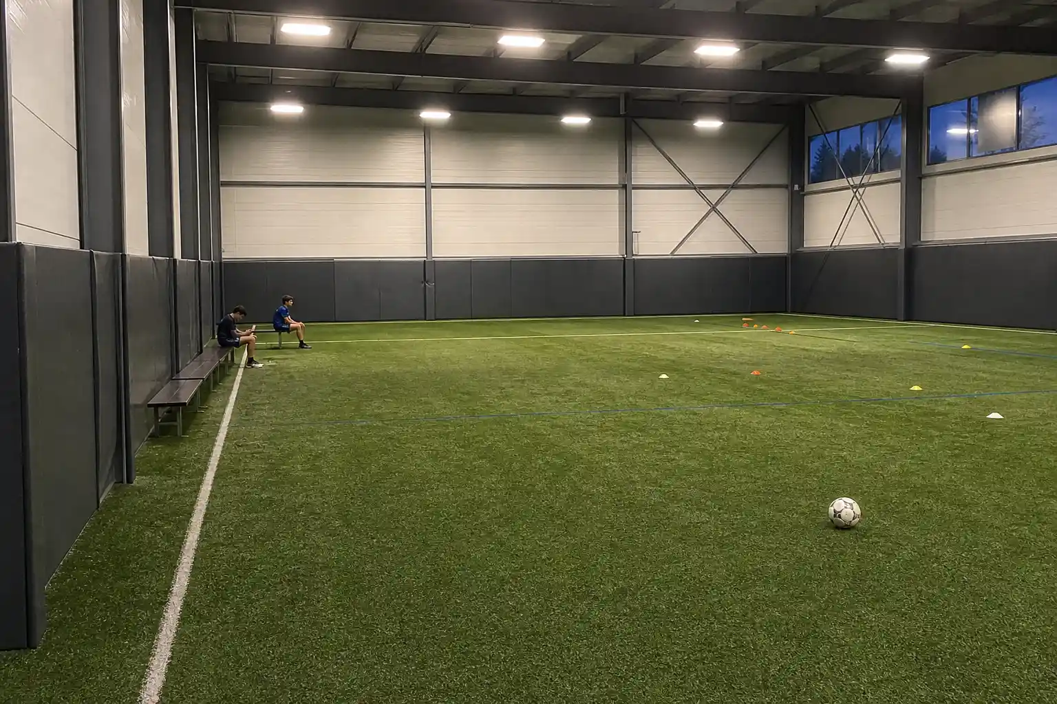 Tom inomhusarena för fotbollsträning med några unga spelare vid bänken i bakgrunden, relaterat till spelproblem bland unga...